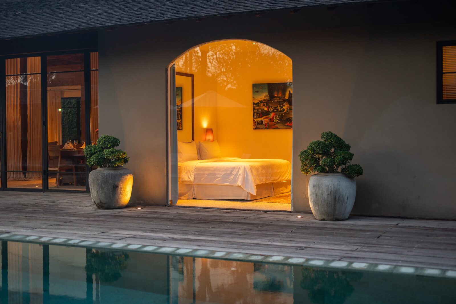 A bedroom glowing through its arched doorway, reflected in the pool at night