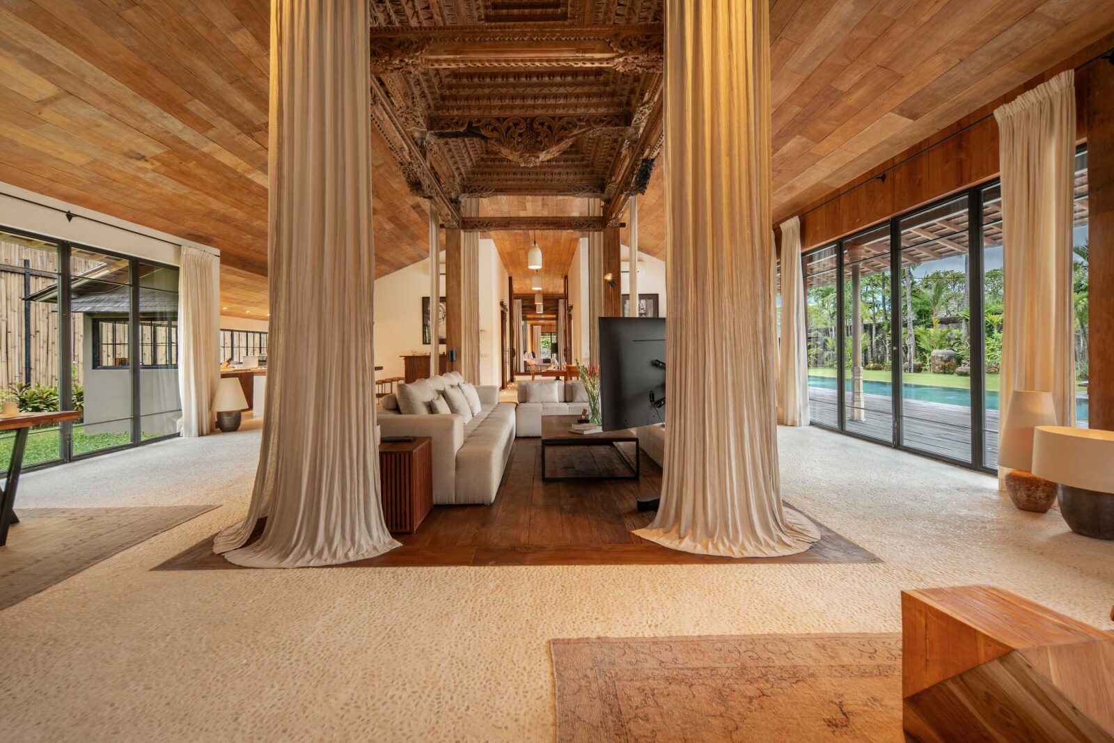 The open-plan living room beneath a carved teak beam, framed by timber columns