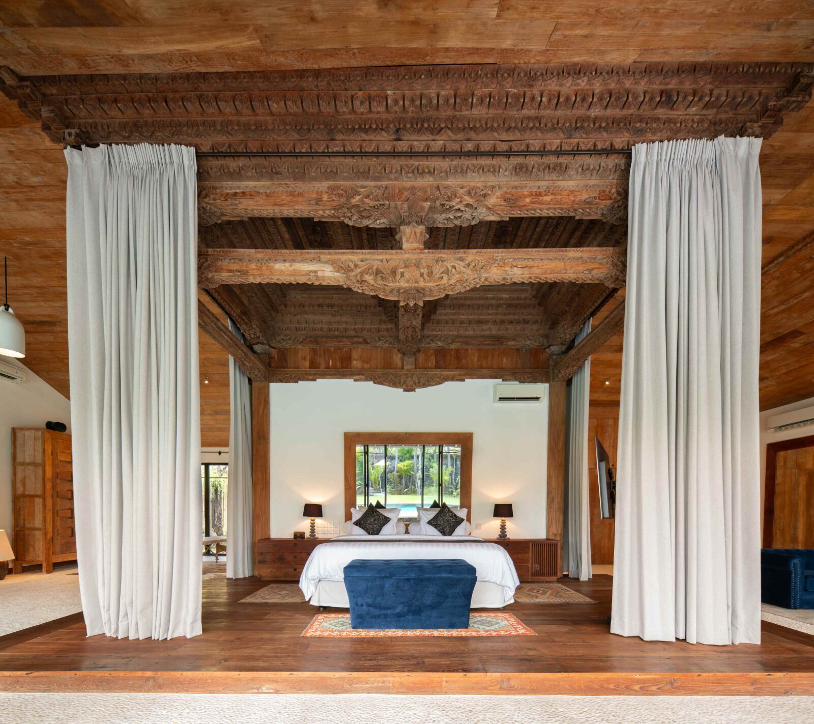 The grand master suite bed beneath a carved teak beam